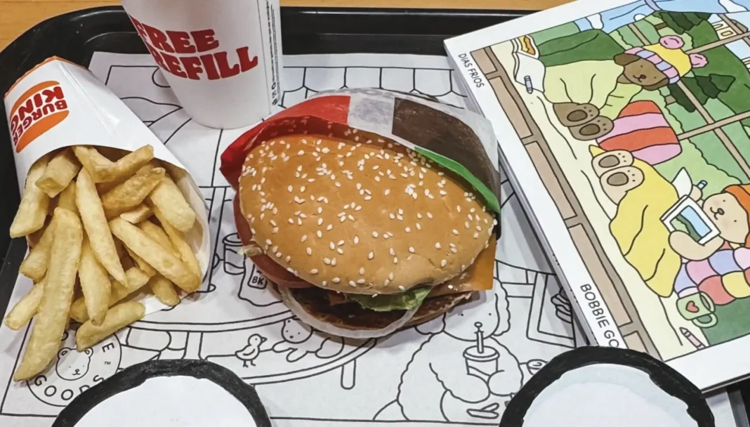 Combo do Burger King com sanduíche, batata média, refrigerante com free refill e o livro de colorir “Bobbie Goods – Dias Frios” ao lado, em uma bandeja ilustrada.
