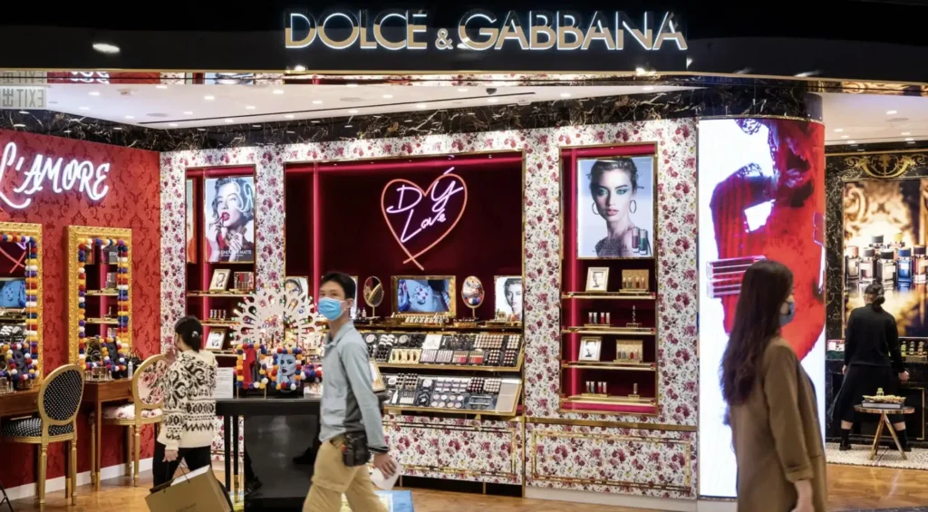 Fachada elegante da loja Dolce & Gabbana Beauty, com vitrine iluminada, logo dourado e decoração sofisticada que destaca os produtos de maquiagem.