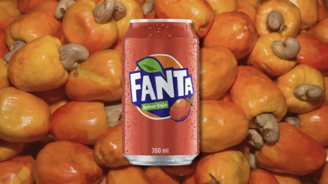Fanta sabor caju sobre um monte de frutas de caju frescas.