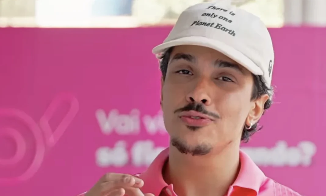 Chico Moedas sorrindo, usando boné rosa e camisa rosa, com fundo rosa.