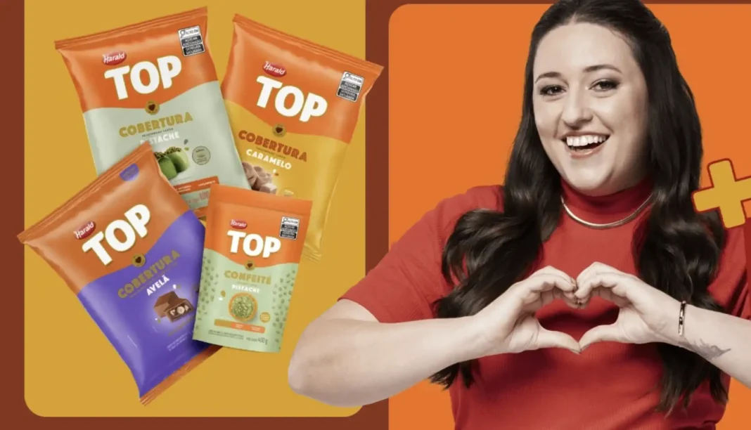 Uma mulher de blusa vermelha sorri e faz um formato de coração com as mãos ao lado de quatro embalagens de produtos de confeitaria da marca Harald Top.