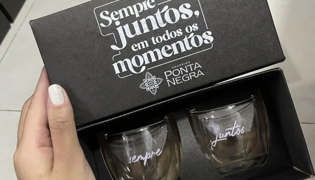 Uma caixa de presente preta aberta revelando duas canecas de vidro. A caixa tem a frase 