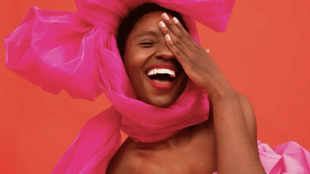 Mulher negra sorrindo com um grande laço rosa na cabeça, cobrindo um olho