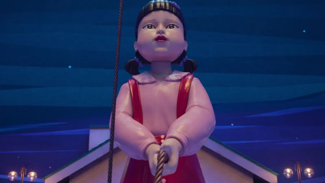 Uma boneca gigante com cabelo escuro, vestido rosa e suspensórios vermelhos, segurando uma corda. Ela está em um cenário noturno com um céu azul escuro.