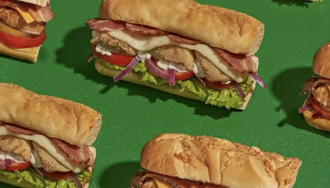 Esta imagem mostra uma variedade de sanduíches Subway dispostos sobre uma superfície verde vibrante.