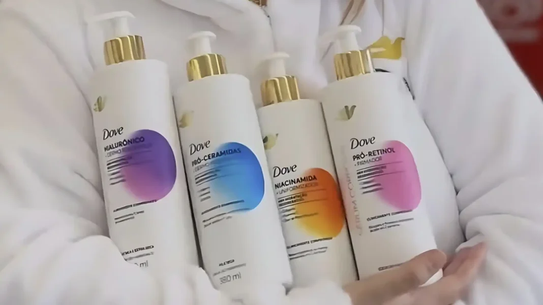 Quatro frascos brancos de loção Dove Body Serum, cada um com uma tampa dourada e um rótulo circular de cor vibrante (roxo, azul, laranja e rosa), sendo segurados por uma pessoa vestindo um roupão branco.