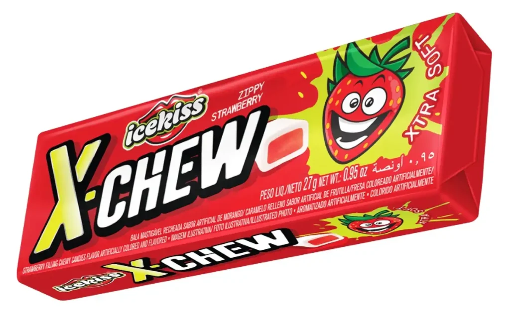 Uma embalagem retangular vermelha e branca de balas X-Chew. A embalagem mostra o logotipo "icekiss X-CHEW" em branco com um contorno amarelo, e "ZIPPY STRAWBERRY" abaixo. À direita, há uma ilustração de um morango sorridente com olhos grandes e bochechas rosadas. Há também um texto em árabe e um texto que diz "SOFT" e "XURA". O peso líquido é indicado como 27g / 0.95 oz. Na parte inferior, há texto em português, inglês e espanhol descrevendo o produto como um doce mastigável de morango. Uma bala mastigável individual branca com recheio vermelho é visível no centro da embalagem.