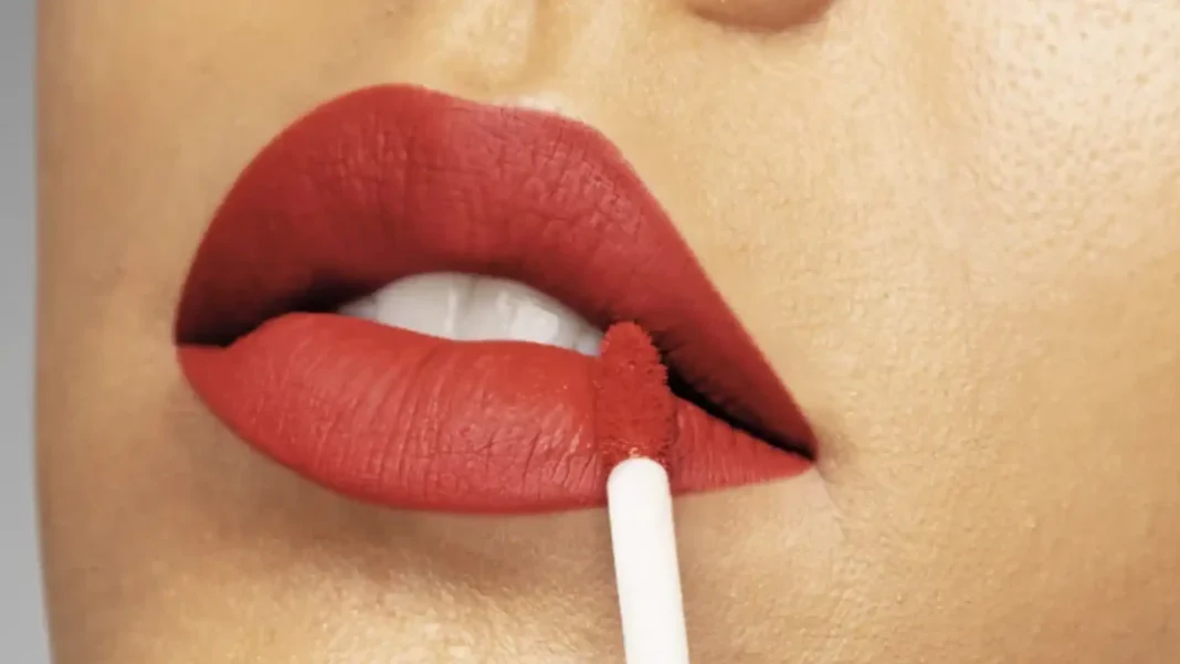 Mulher aplicando batom vermelho matte líquido nos lábios.