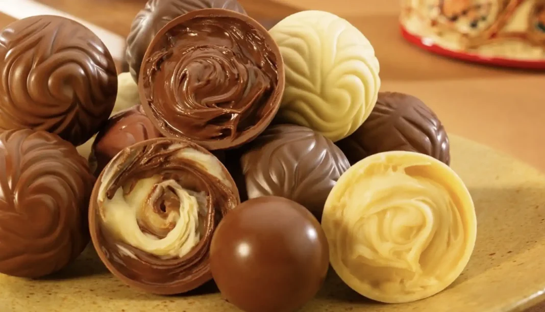 Uma pilha de trufas de chocolate de vários tipos e recheios, algumas cortadas ao meio revelando recheios cremosos.