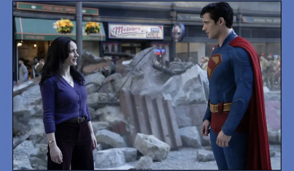 Uma foto de Superman (interpretado por David Corenswet) em seu traje clássico azul e vermelho com uma capa, de perfil, olhando para Lois Lane (interpretada por Rachel Brosnahan). Ela está vestindo um cardigã roxo sobre uma blusa mais clara e calças escuras, com cinto, e também está de perfil, olhando para ele. Eles estão parados em uma rua com destroços, possivelmente de um conflito, ao fundo. Ao fundo, pode-se ver edifícios e algumas pessoas, dando a entender que estão em uma cidade.