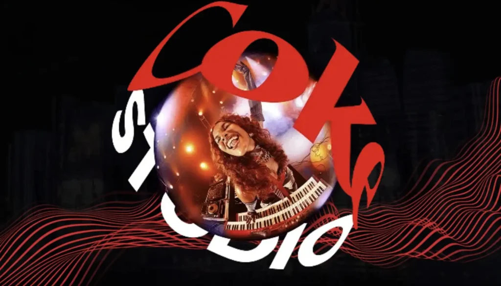 
Uma imagem apresenta o logotipo "Coke Studio" em vermelho e branco, sobreposto a um fundo escuro com ondas sonoras vermelhas. Dentro da letra 'o' de "Coke", há uma esfera brilhante com uma mulher de cabelo ruivo e encaracolado sorrindo e tocando um teclado.