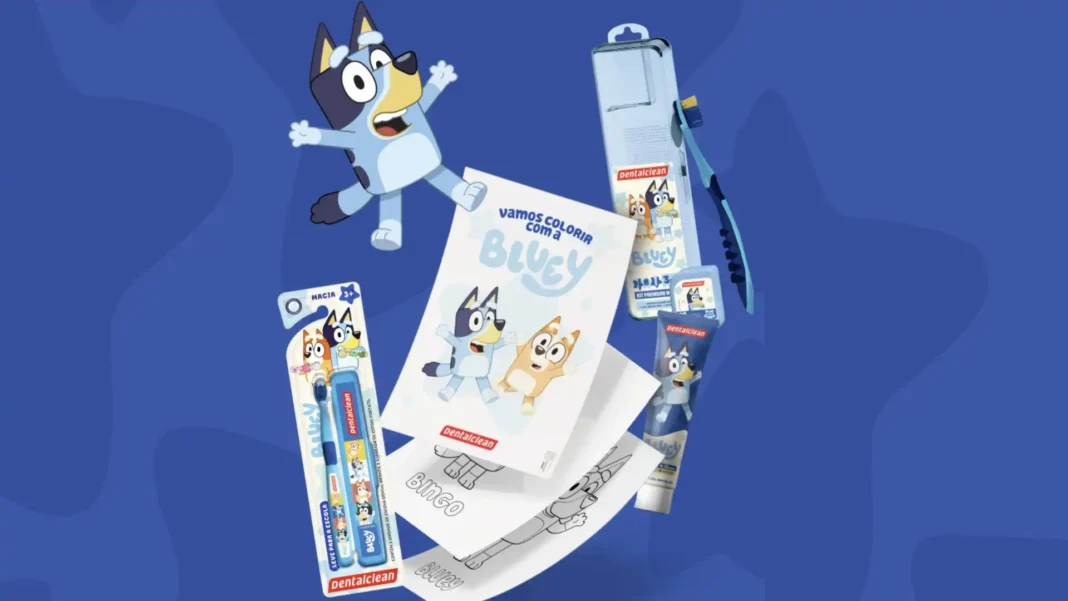 Um banner promocional da Dentalclean com personagens da série animada Bluey. Um desenho do Bluey corre no canto superior esquerdo. No centro, há um livro de colorir aberto com a frase 'Vamos Colorir com a Bluey'. Abaixo do livro, há folhas com desenhos de personagens da Bluey para colorir. No lado esquerdo, uma escova de dentes infantil azul com personagens da Bluey é exibida em sua embalagem. À direita, um kit de higiene bucal para crianças, também com a temática Bluey, inclui uma escova de dentes e pasta de dente em uma embalagem transparente, juntamente com uma pasta de dente avulsa. O fundo é azul.