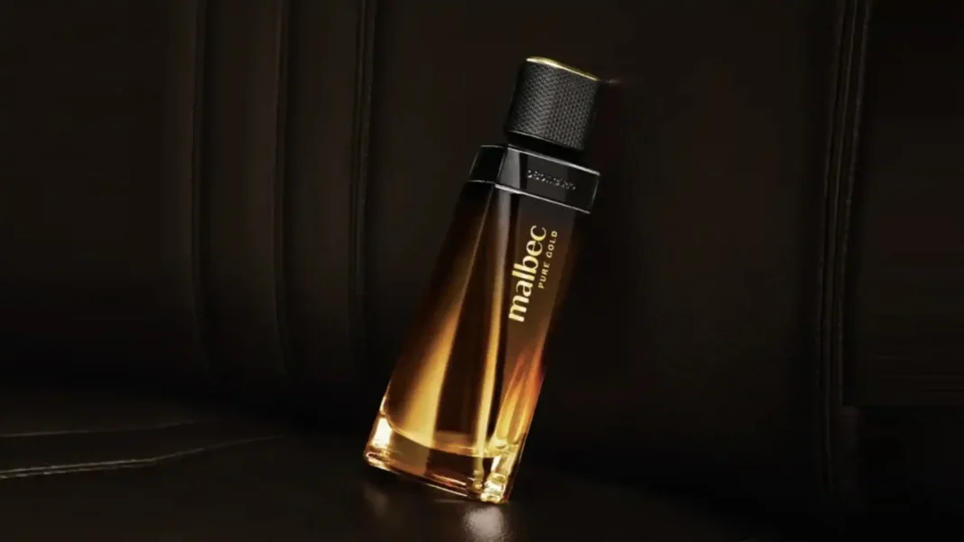 Frasco de perfume Malbec Pure Gold com líquido dourado inclinado sobre um fundo escuro e texturizado.