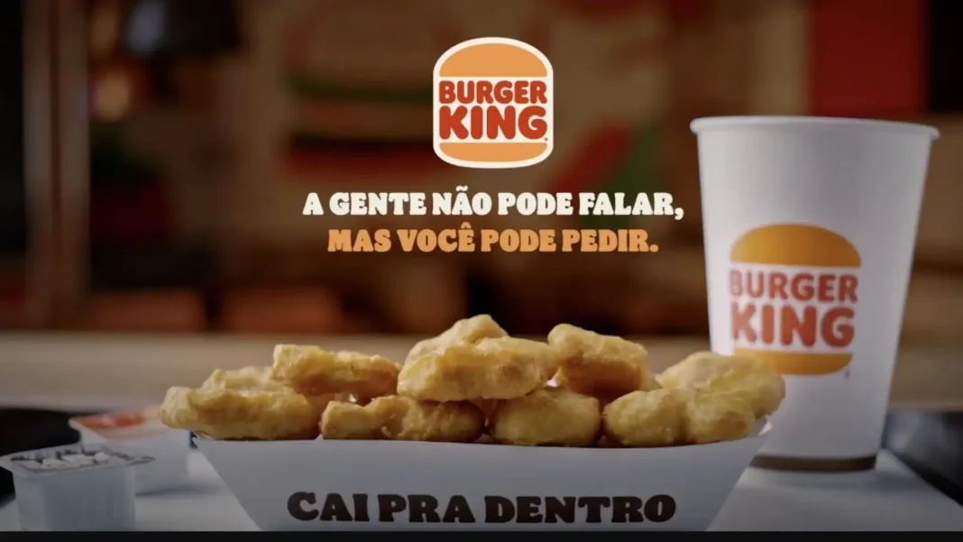 Uma bandeja de nuggets de frango do Burger King com um copo e molho em um fundo desfocado. O texto na tela diz 
