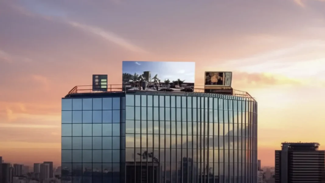 Um arranha-céu de vidro com duas telas exibindo cenas de filmes e um banner no topo ao pôr do sol.