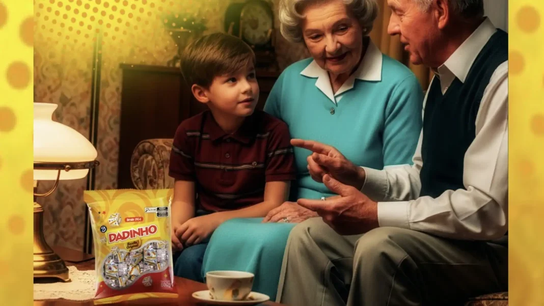 Um menino jovem senta-se num sofá entre uma mulher idosa e um homem idoso, todos olhando para o homem, com um saco de doces Dadinho em primeiro plano.