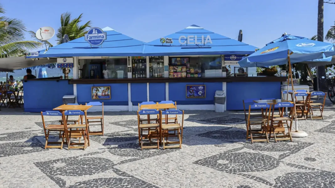 Um quiosque de praia azul claro com a marca Farmina Pet Foods e mesas de madeira em uma calçada de mosaico de pedras portuguesas.
