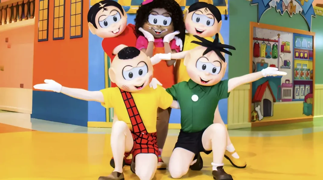 Mascotes da Turma da Mônica em um palco com cenário colorido.