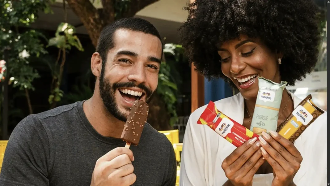 Um casal sorridente desfruta de picolés da marca Frisabor. O homem come um picolé coberto de chocolate e amendoim, enquanto a mulher segura três embalagens de diferentes sabores.