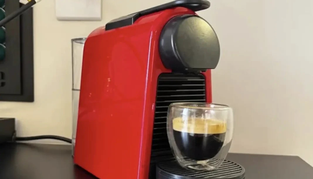 Uma máquina de café Nespresso vermelha com uma xícara de café cheia.