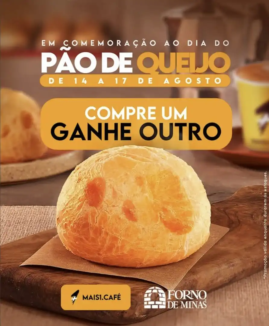 Um pão de queijo grande e dourado em primeiro plano, sobre uma tábua de madeira com papel marrom.