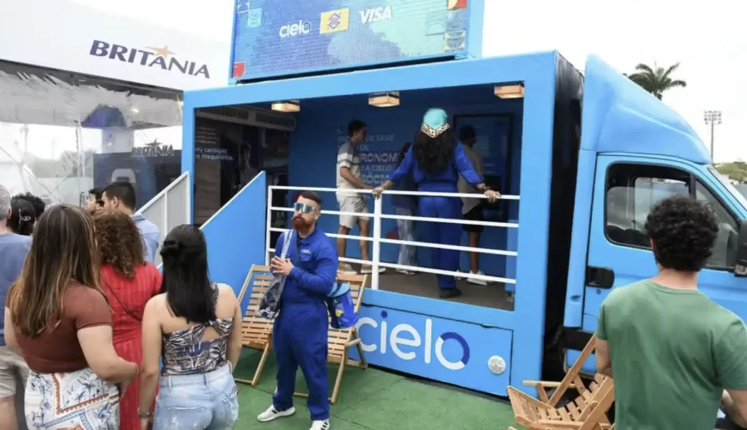 Um grupo de pessoas está reunido em frente a um caminhão azul que serve como estande da Cielo e aceita pagamentos Visa.