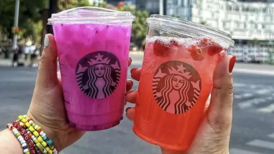 Dois copos de Starbucks Dragon Drink com gelo e pedaços de fruta do dragão em um balcão claro contra uma parede bege.