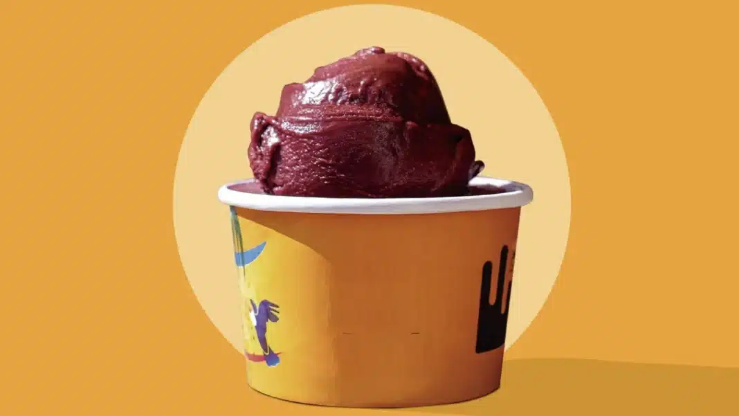 Pote de açaí com uma grande porção de açaí cremoso no topo, com fundo laranja e um círculo branco.
