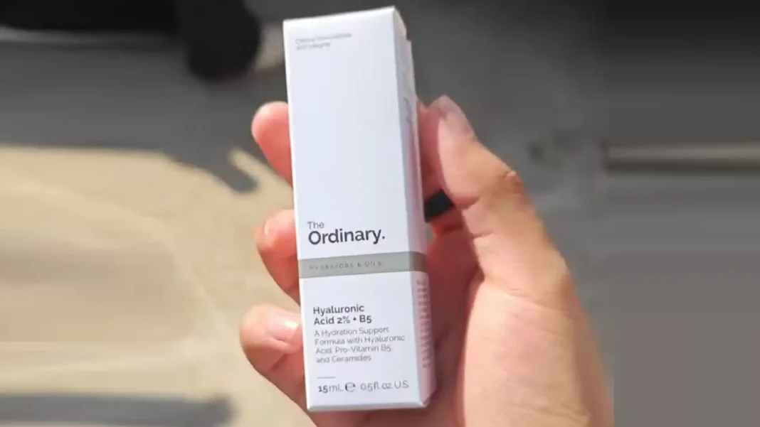 Uma mão segurando uma caixa branca de The Ordinary, um produto de cuidados com a pele.
