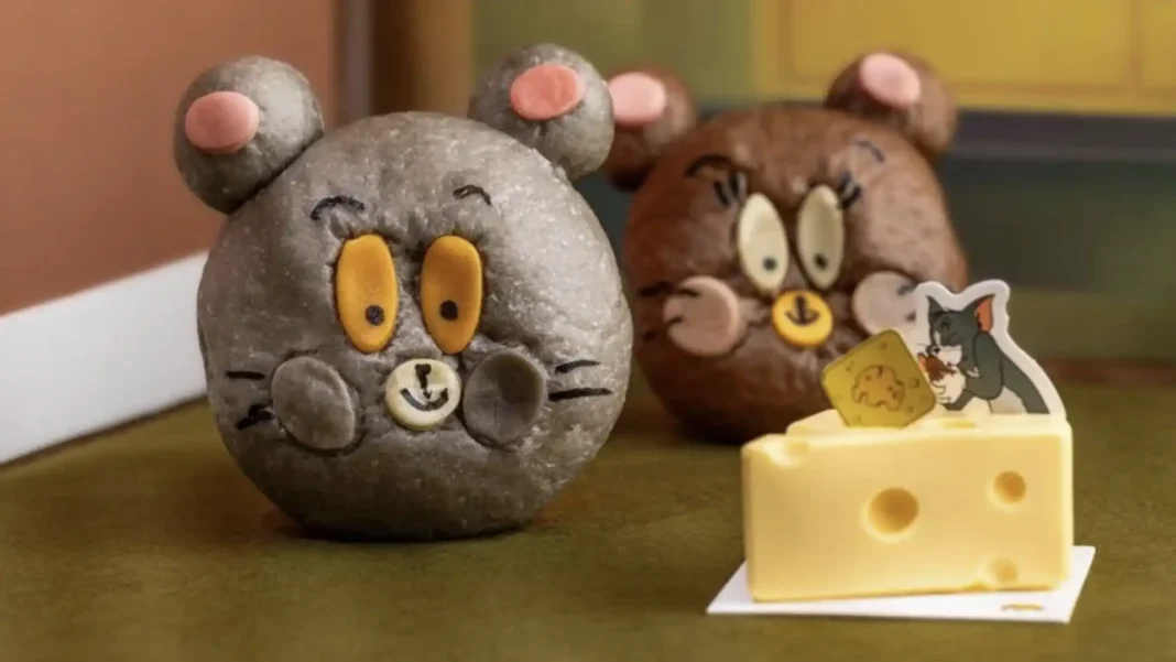 Dois pães em formato de cabeça de rato, representando Tom e Jerry, ao lado de um bolo em formato de queijo.