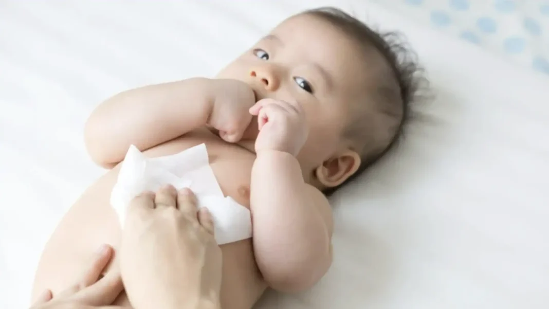 Mão de adulto usando um lenço umedecido para limpar a barriga de um bebê.
