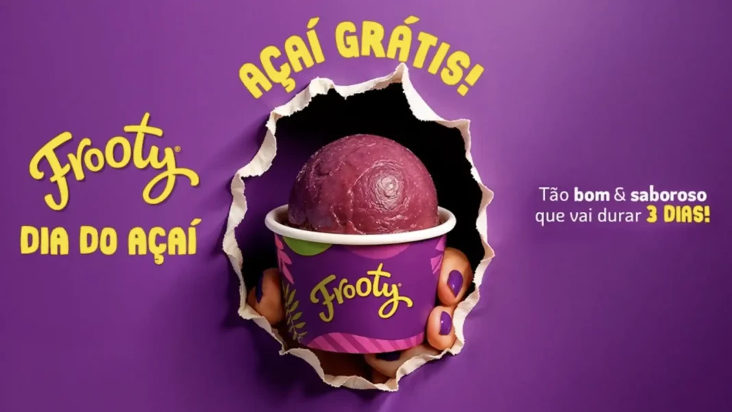 Um pote de açaí roxo da marca Frooty, visto de perto e segurado por mãos com unhas pintadas de roxo.