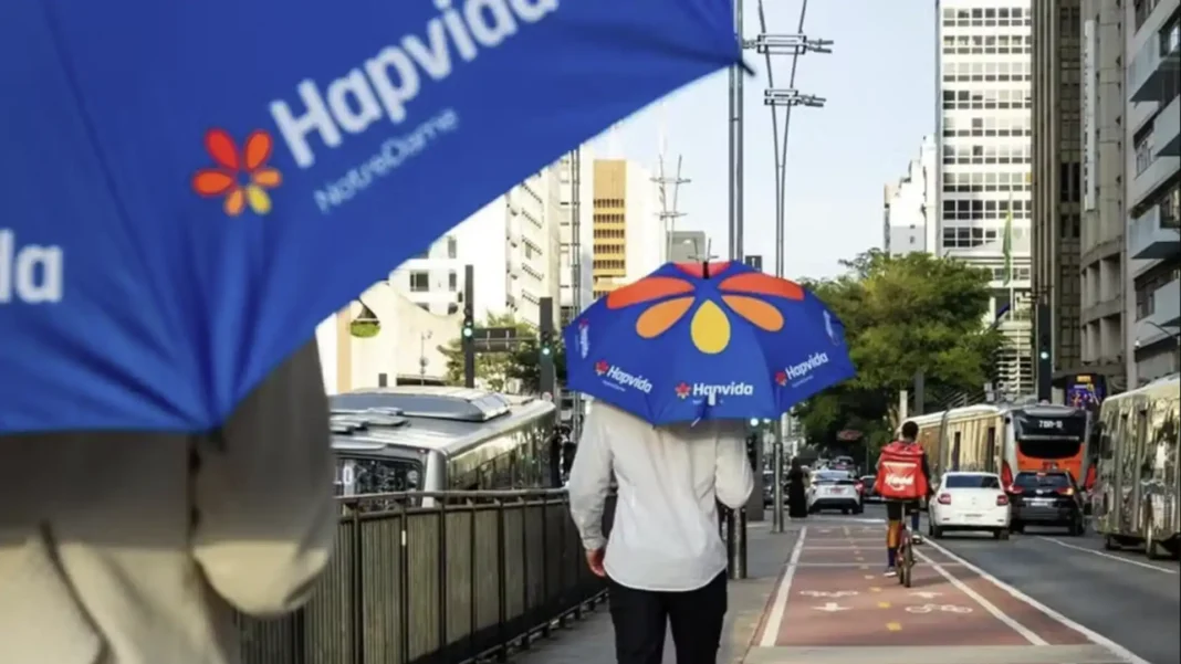 Pessoas usando guarda-chuvas azuis com o logotipo da Hapvida na rua.