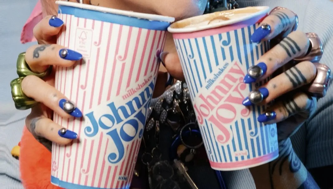 Duas mãos, com anéis e tatuagens, seguram dois milkshakes da marca 