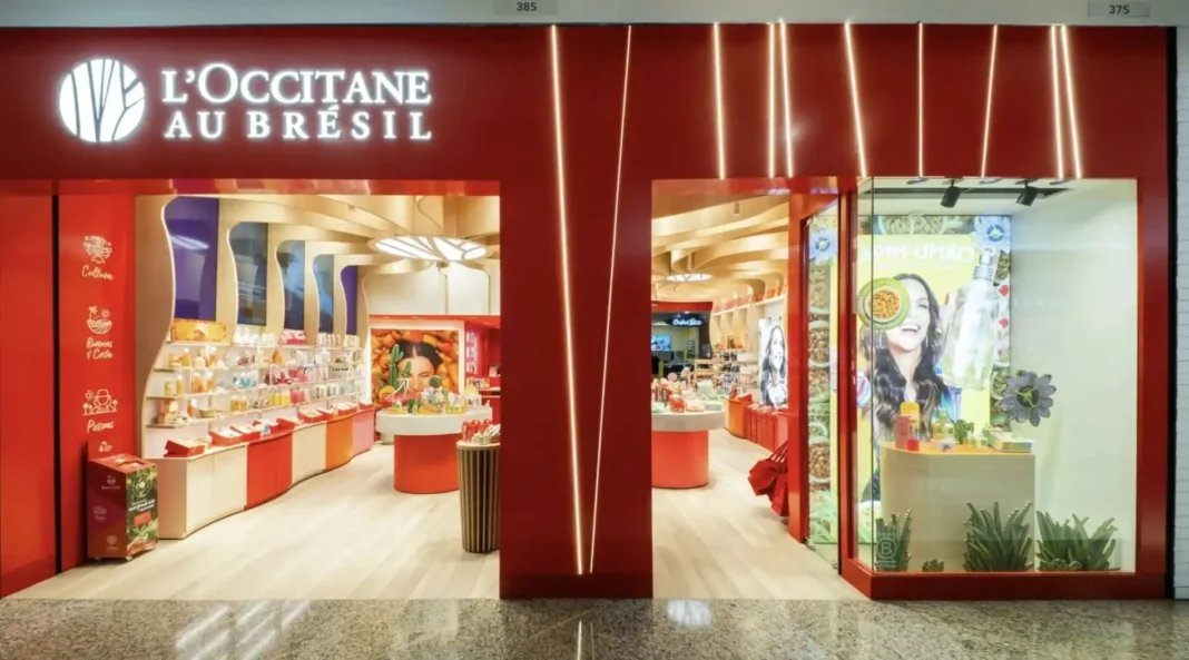 A fachada da loja L'OCCITANE AU BRÉSIL no Shopping Morumbi. O letreiro é branco sobre um fundo vermelho vibrante. A loja tem duas entradas amplas, com paredes e prateleiras internas em tons de madeira e vermelho, exibindo diversos produtos de beleza e cuidados pessoais.