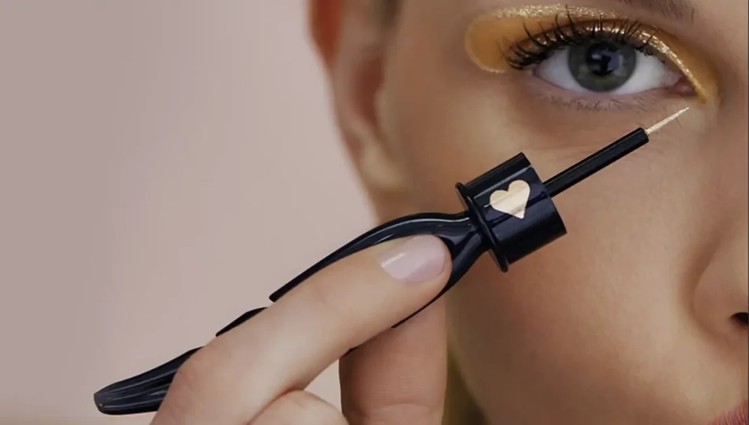 Um close-up de uma mulher aplicando um delineador de glitter dourado na pálpebra superior.