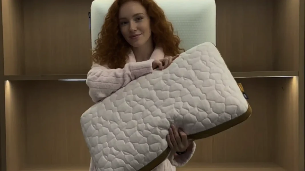 Mulher ruiva com pijama rosa segurando um travesseiro branco com textura de colmeia.