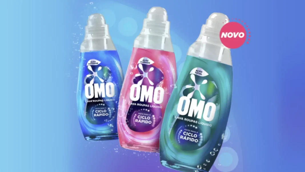 Três garrafas de OMO líquido para roupa, nas cores azul, rosa e verde-água, sobre um fundo azul com bolhas. A garrafa azul está à esquerda, a rosa no centro e a verde-água à direita. Todas têm um rótulo com a inscrição 'OMO Lava Roupas Líquido Feito para o Ciclo Rápido'. Há um selo vermelho no canto superior direito com a palavra 'NOVO'.