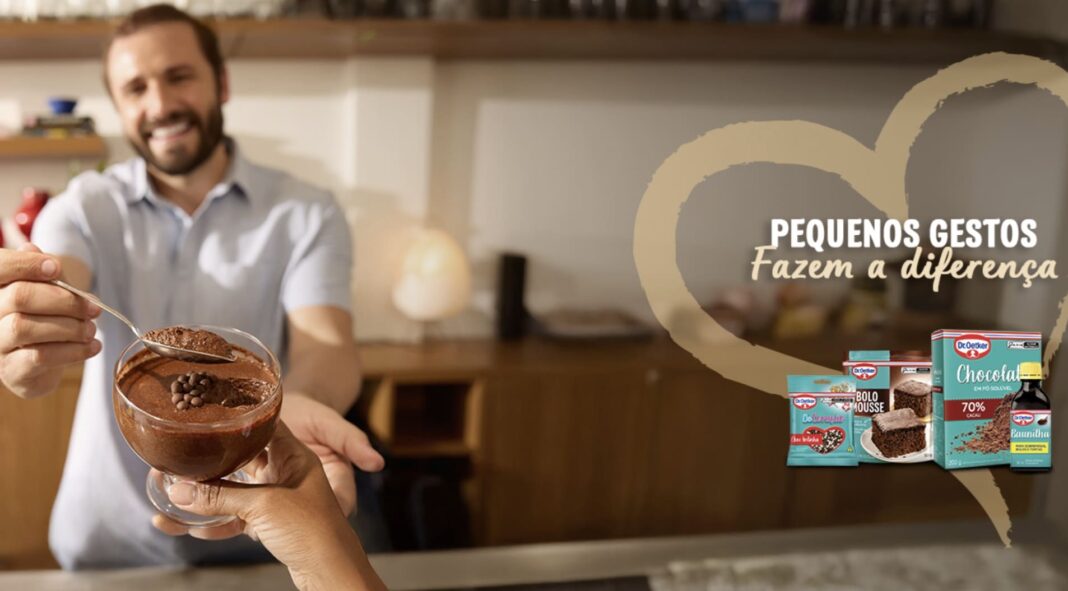 Homem sorridente oferece mousse de chocolate em tigela de vidro.