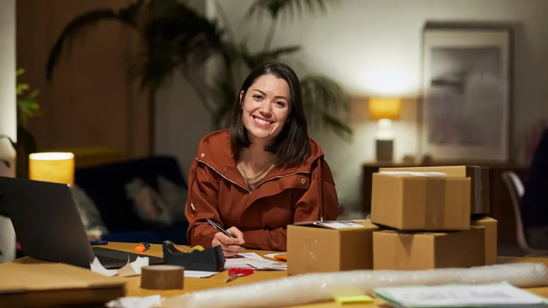 Mulher sorridente em mesa com caixas e material de embalagem.