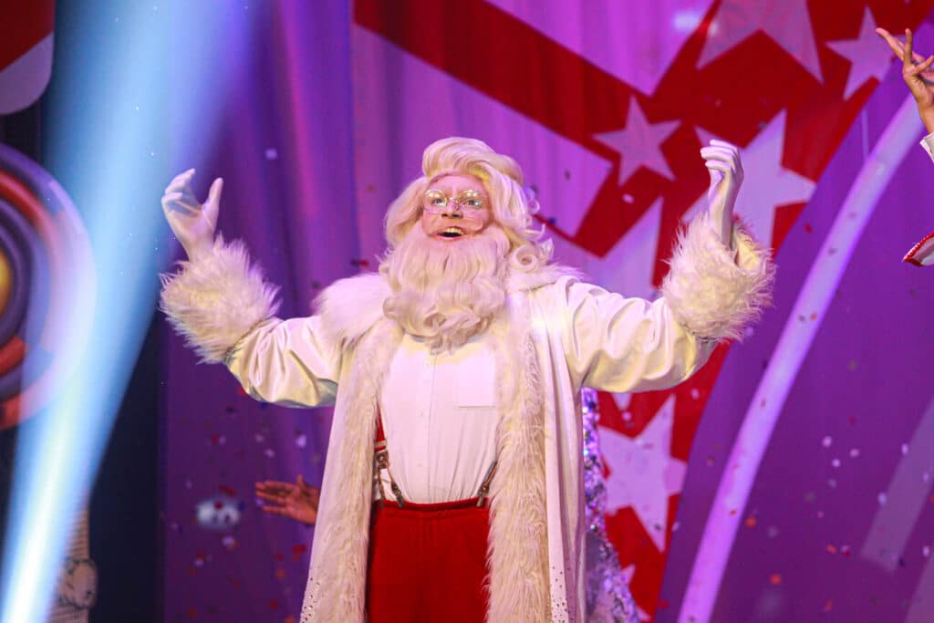 Natal Mágiko 2025 Hopi Hari se transforma em vila encantada com entrada gratuita para crianças Papai Noel com barba e cabelo loiros e traje branco com detalhes de pelo, gesticulando no palco.