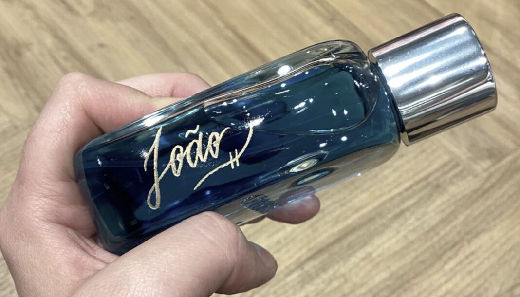 Frasco de perfume azul-escuro segurado por uma mão, com o nome 