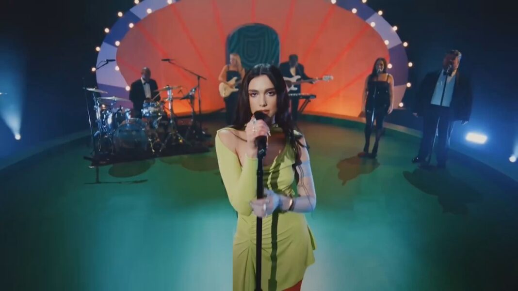 Dua Lipa se apresentando no palco com uma roupa verde-limão e banda ao fundo.